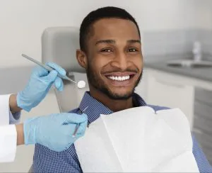 young adult man smiling in the dental chair as the dentist uses tools to examine his mouth